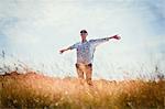 Carefree senior woman running with arms outstretched in sunny field