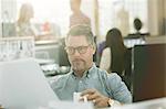 Fashion designer reviewing paperwork and drinking coffee in office