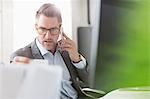 Businessman examining paperwork talking on cell phone in office