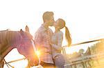 Affectionate couple kissing next to horse in sunny rural pasture