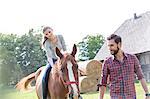 Man leading woman horseback riding in rural pasture