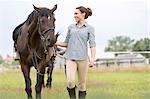 Smiling woman walking horse in rural pasture