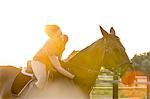 Woman on horseback petting horse in rural pasture