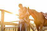 Couple with horse hugging in sunny rural pasture