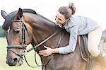 Smiling woman horseback riding leaning and petting horse