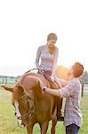 Smiling couple horseback riding in rural pasture