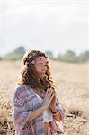 Serene boho woman meditating with hands at heart center in sunny rural field