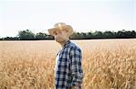 Man wearing a checked shirt and a hat standing in a cornfield, a farmer.