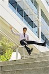 Young and happy chinese businessman sliding downstairs on rails of office staircase. The man enjoys his new promotion at job
