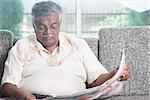 Elder Indian man reading newspaper at home. Asian senior people living lifestyle indoors.