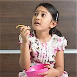 Cute Indian girl eating traditional snack murukku. Asian child enjoying food, living lifestyle at home.