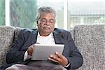 Modern technology. Old Indian man using touch screen tablet computer at home. Asian senior people living lifestyle indoors.