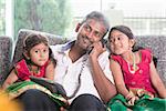 Husband making a phone call to wife while taking care of children at home. Asian Indian family at home.