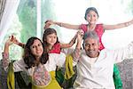 Happy Indian family at home. Asian parents playing with their kids, sitting on sofa. Parents and children indoor lifestyle.