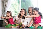 Happy Indian family at home. Asian people laughing and pointing to somewhere. Parents and children indoor lifestyle.