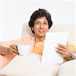 Portrait of a 50s Indian mature woman using tablet computer at home. Older people, modern technology concept. Indoor senior people living lifestyle.
