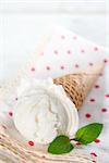 Scoop milk ice cream in waffle cone with mint on wood background.