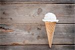 Single vanilla ice cream in a waffle cones over wooden background with copy space.