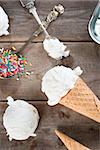 Top view scoop vanilla ice cream in waffle cone with spoon and color rice on wood background.