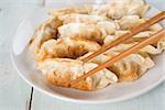 Close up fresh pan fried dumplings on plate with chopsticks and hot steams. Asian food on rustic vintage wooden background.