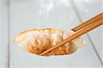 Close up fresh pan fried dumplings with chopsticks and hot steams. Asian food on rustic vintage wooden background.