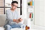 Portrait of casual 50s mature Asian man wrist pain, pressing on wrist with painful expression, sitting on sofa at home, medicines and water on table.