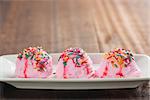 Pink ice cream on plate, decor with colorful rice, copy space on top, on old wooden vintage table background.