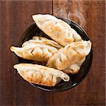 Top view fresh pan fried dumplings on bowl. Chinese dish with hot steams on rustic vintage wooden background.