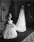 1950s LITTLE FLOWER GIRL MAID OF HONOR BACK TO CAMERA FOLLOWING WEDDING COUPLE HOLDING EDGE OF LACE VEIL TRAIN