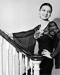 1930s WOMAN WEARING SPANISH STYLE DRESS WITH LACE & FULL CHIFFON SLEEVES SMILING STANDING ON STAIRCASE LOOKING BACK