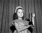 1950s 1960s YOUNG GIRL STANDING WITH TROPHY LOVING CUP WEARING TIARA PRETTY DRESS WINNER OF BEAUTY PAGEANT LOOKING AT CAMERA