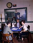 1960s COLLEGE RADIO STATION DJ INTERVIEWING MAN & WOMAN AROUND MICROPHONE AT TABLE ON AIR SIGN CONTROL ROOM BROADCASTING