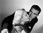 1950s 1960s COUPLE ALOOF WOMAN PRETTY BLONDE HAIR ELEGANT EARRINGS FASHION PROFILE ABOUT TO BE KISSED BY MAN STANDING BEHIND HER