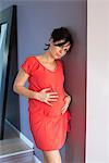 Pregnant woman leaning against wall with hands on stomach, portrait