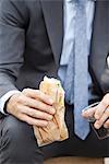 Businessman holding sandwich, cropped