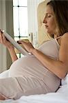 Pregnant woman lying in bed using digital tablet
