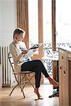 Young woman reading newspaper at home