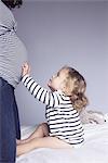 Little girl touching mother's pregnant stomach, cropped