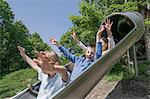 Three friends sliding down on slide in playground, Munich, Bavaria, Germany