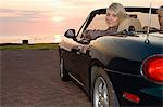 Woman sitting in convertible at sunset