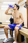 Man drinking water on locker room bench