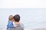 Father and young son looking at sea view, rear view