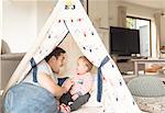 Father and young son sitting in play tent indoors, laughing together