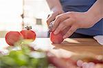 Hands of woman slicing tomato at kitchen counter