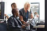 Young woman in hair salon wearing hair cutting cape choosing hair dye colour from swatches