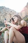 Young man and teenage sister reading smartphone texts on rocky beach, Javea, Spain