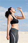 Mid adult woman drinking from water bottle whilst exercising  at beach