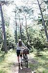 Mature woman pushing bicycle with foraging baskets on forest path