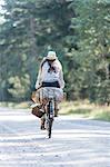 Rear view of woman cycling on forest road with foraging baskets