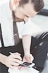 Businessman sitting cross legged making diary notes from smartphone outside office